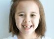 Young girl smiling at camera against light blue background, dental portrait.