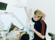 Dentist in mask assists patient in modern dental clinic treatment room.