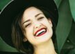 Woman wearing black hat smiling against green background for dental studio portrait
