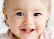 Smiling toddler with blonde hair wearing pink shirt against white background.
