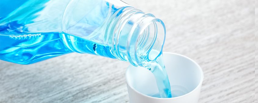 Water pouring from plastic bottle into white cup on wooden surface