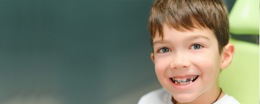 Young boy smiling at camera in dental office setting with green background