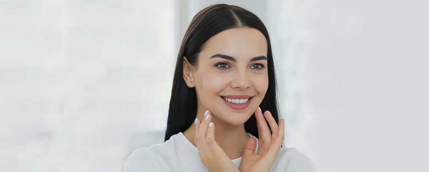 img-microsurgery Woman smiling while touching her face against white background, dental care setting.