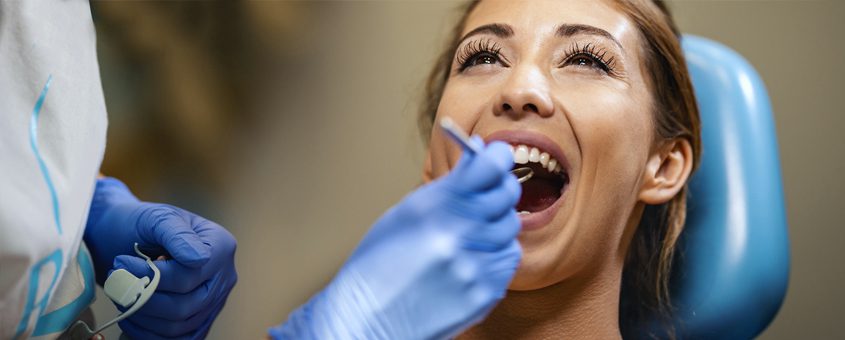 Woman receiving dental examination in dental chair with dentist wearing blue gloves.