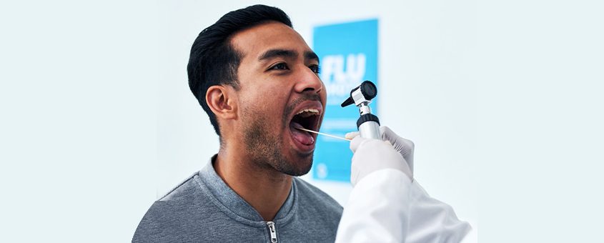 Man in gray shirt pointing at blue dental diagram on white wall at dental studio.