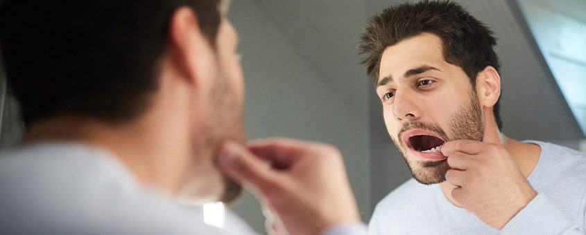 Man brushing teeth at bathroom mirror in dental care routine.