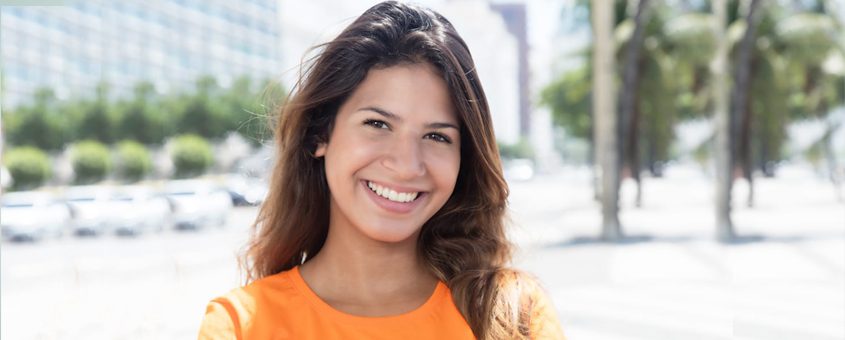img-pdo-smooth-threads Smiling woman in orange shirt outdoors with blurred urban background and palm trees