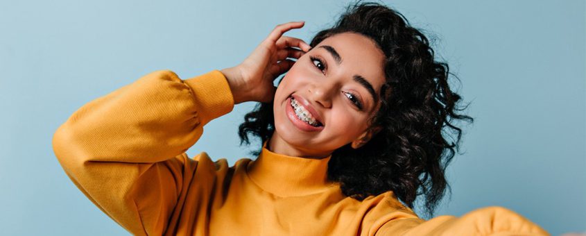 img-powerprox-6-month-braces Smiling woman in yellow sweater touching head against blue background studio portrait