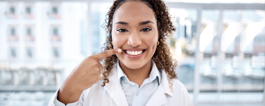 img-root-resorption Smiling dental professional in white coat touching face in modern office setting.