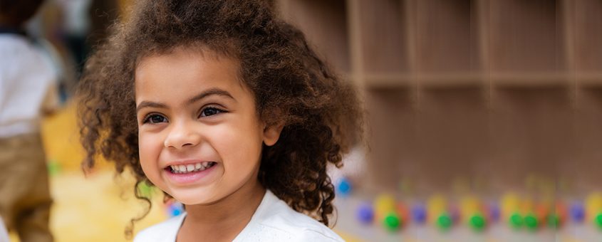 Young child smiling at camera in bright dental office setting with colorful background.