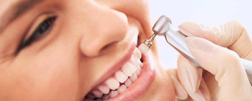 Dentist performing professional teeth cleaning on smiling patient in dental clinic setting.