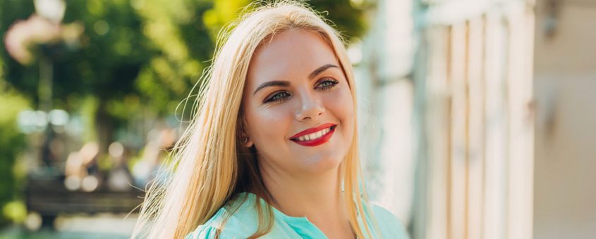 Professional woman with blonde hair smiling outdoors in casual blue top near building