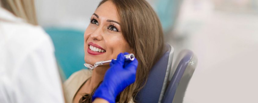 img-the-wand Woman smiling during dental examination wearing blue gloves in dental office setting.