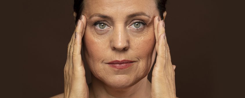 img-wrinkles Woman with blonde hair touching her face against brown background, dental studio portrait.