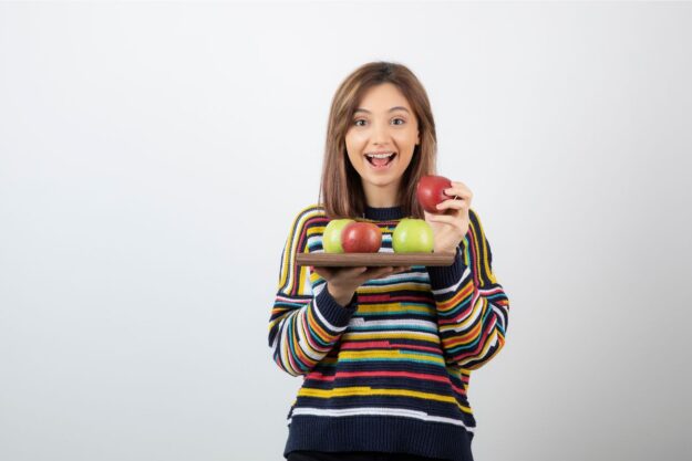 A smiling girl with healthy teeth holding a tray of vitamin-rich fruits, emphasizing enamel health and prevention.