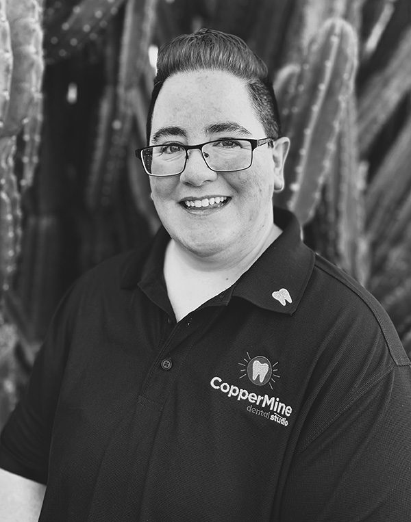 Professional headshot of smiling woman wearing CopperMine Dental Studio branded polo shirt and glasses indoors.