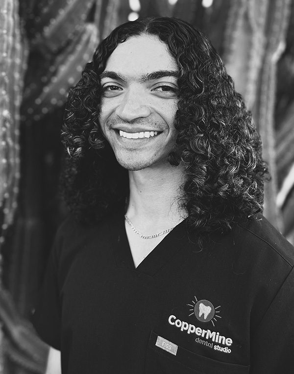 Smiling dental professional in dark CopperMine Dental Studio uniform against textured background.