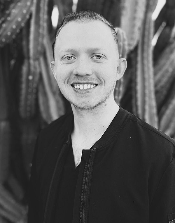 Professional headshot of smiling man in black jacket against blurred background at dental studio.