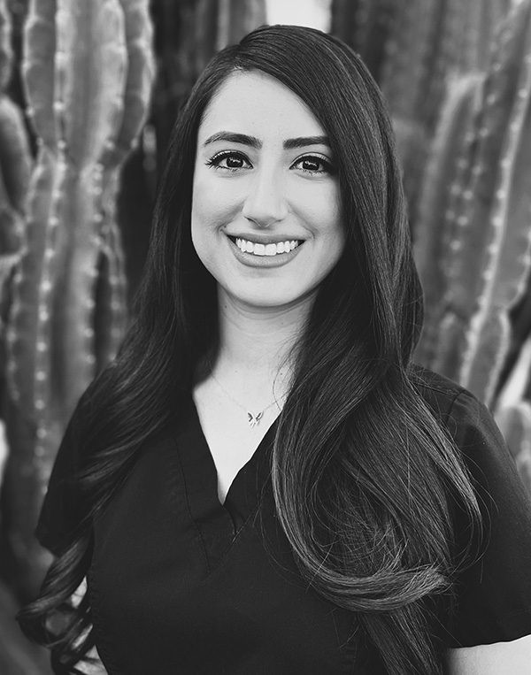 Professional headshot of smiling woman with long dark hair against textured background for dental studio.