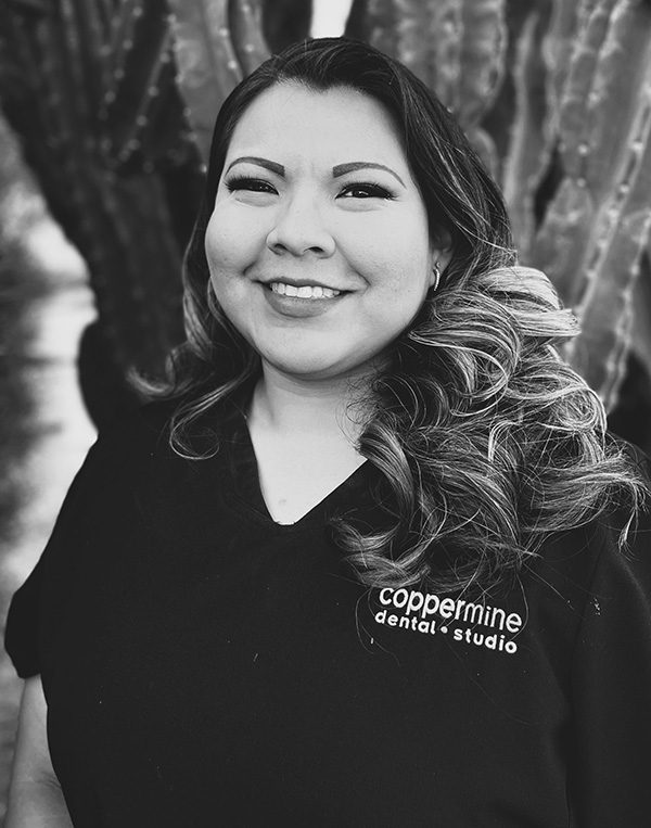 Woman smiling at camera wearing CopperMine Dental Studio branded shirt, black and white portrait.