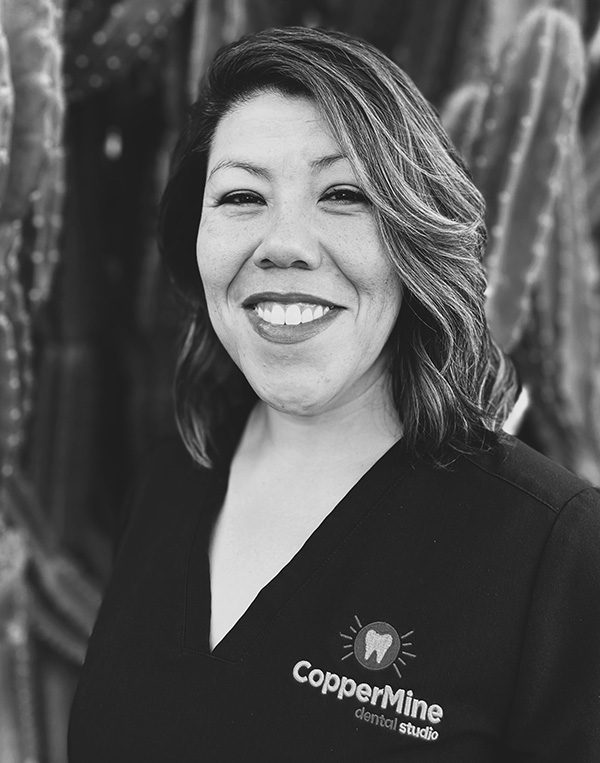 Professional headshot of smiling woman wearing CopperMine Dental Studio branded attire against textured backdrop.