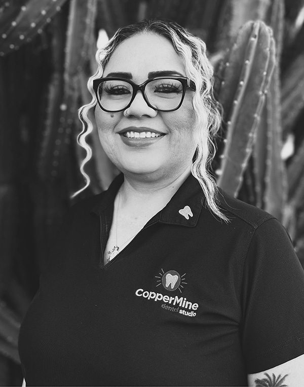 Woman wearing glasses and CopperMine Dental Studio polo shirt smiling at camera in professional portrait.
