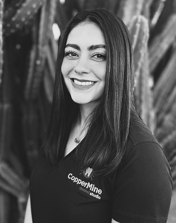 Professional woman smiling at camera wearing CopperMine Dental Studio branded shirt, black and white portrait.