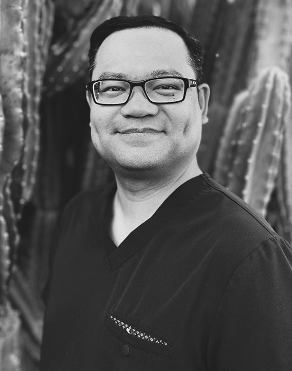Professional headshot of a man wearing glasses and black v-neck shirt against textured background.