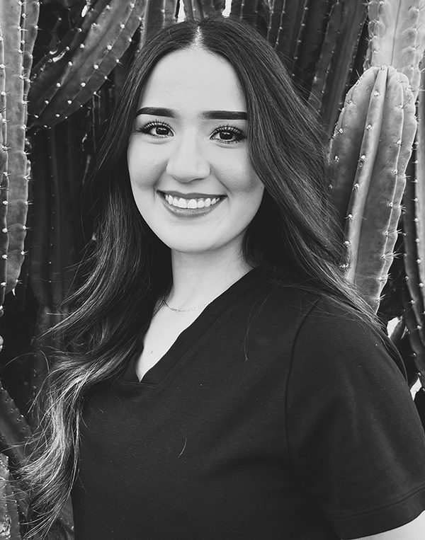 Professional headshot of smiling woman with long dark hair against sparkly backdrop at dental studio.