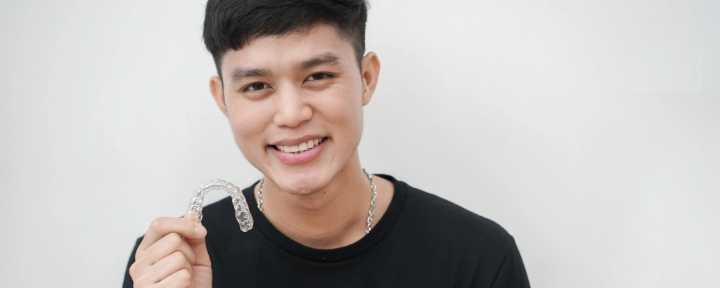 Img-invisalign Young man in black shirt smiling at camera against white background, dental studio portrait