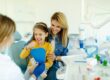 A mother and child interacting with a dentist while the child practices brushing during a routine dental checkup.