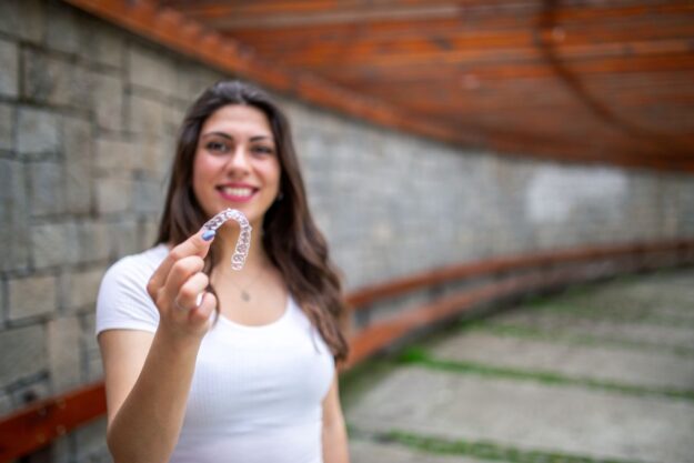 Smiling woman holding a clear retainer after Invisalign treatment to maintain teeth alignment and long-term results.