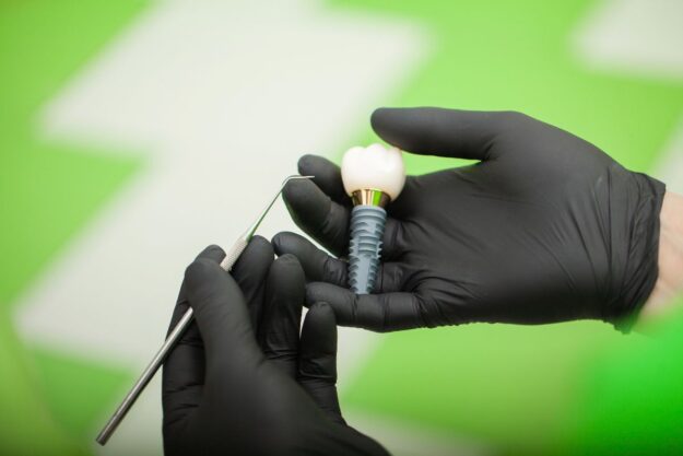 Dental implant held by gloved hands during procedure.
