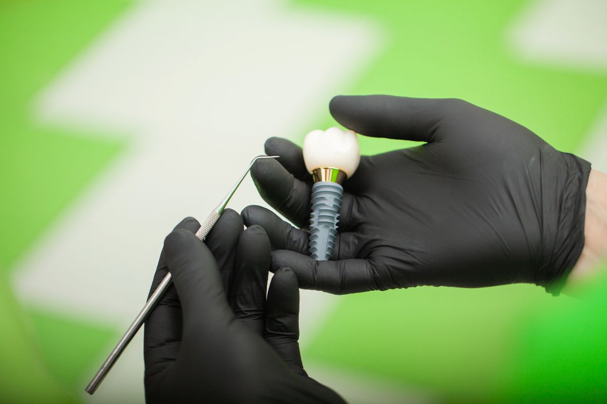 Dental implant held by gloved hands during procedure.