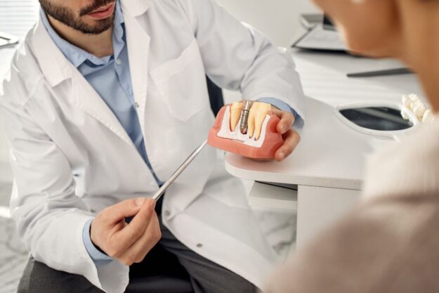 Dentist showing dental implant model during consultation.