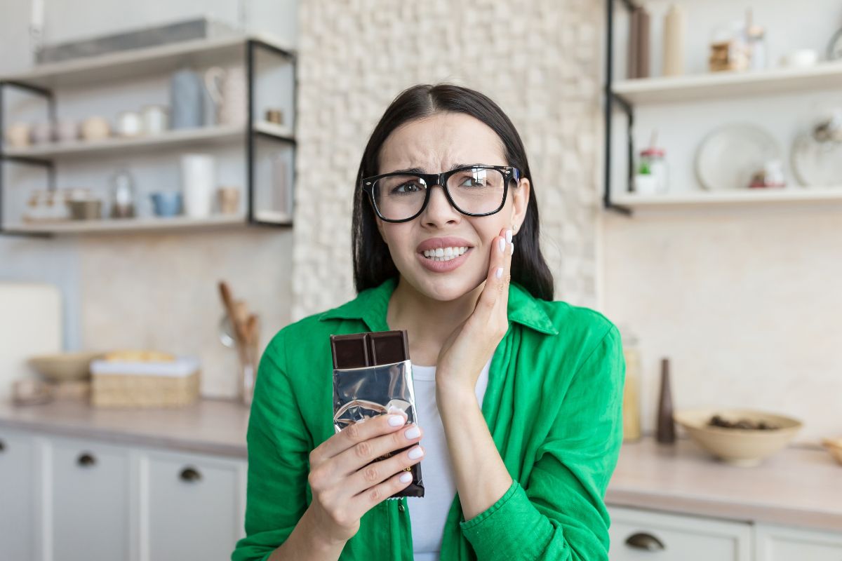 Woman with tooth pain holding a chocolate harmful to teeth.