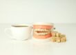 Cup of coffee beside a dental model and sugar cubes, illustrating the harmful effects of sugar on teeth and oral health.