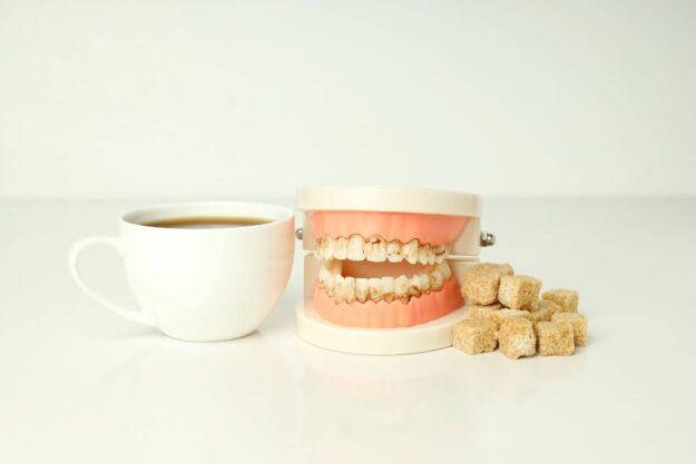 Cup of coffee beside a dental model and sugar cubes, illustrating the harmful effects of sugar on teeth and oral health.