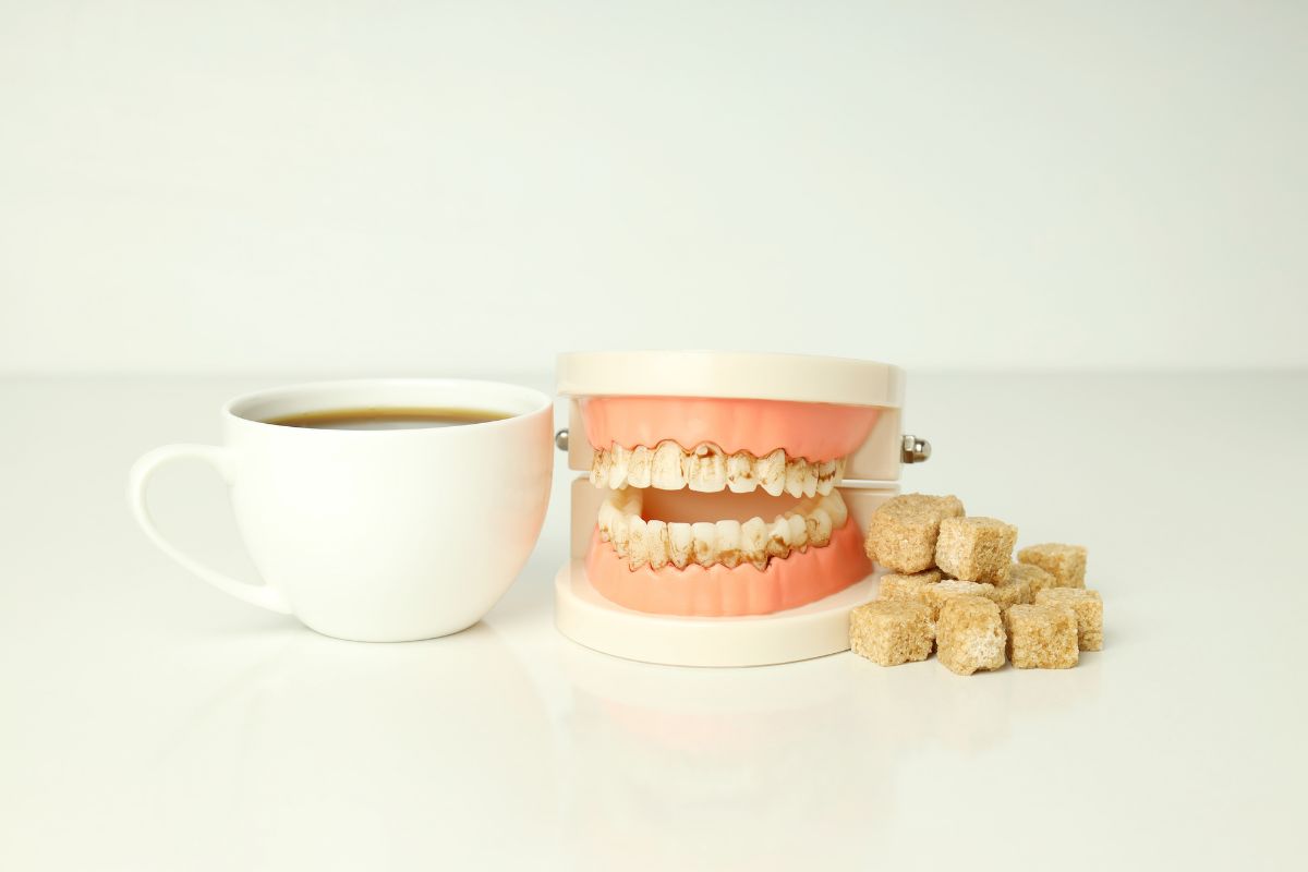 Cup of coffee beside a dental model and sugar cubes, illustrating the harmful effects of sugar on teeth and oral health.